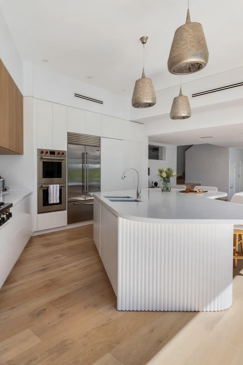 Renovated white kitchen with timber overheads and a curved island